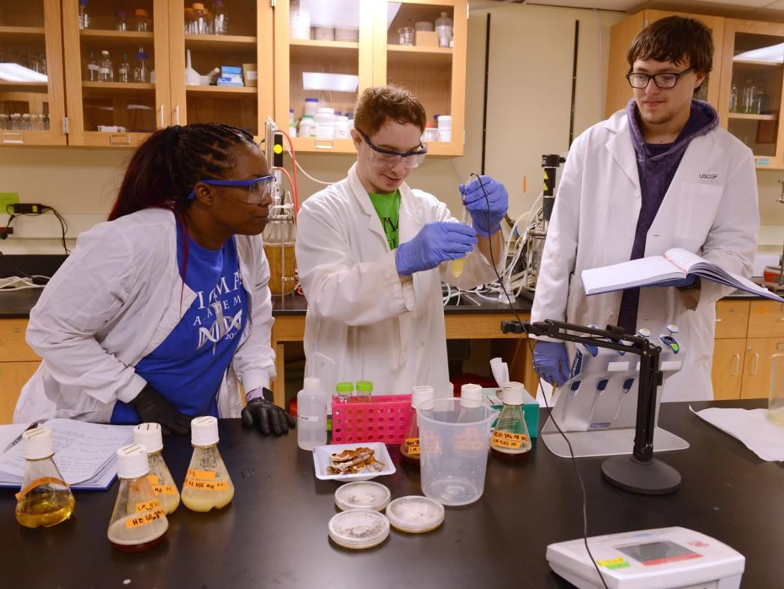 Three students in a lab reviewing the contents of beakers