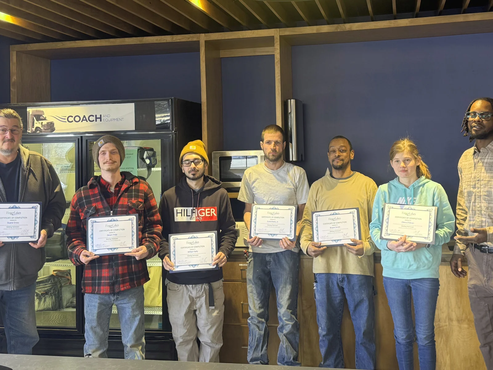 An instructor stands next to a man in a welding helmet using computer simulation technology