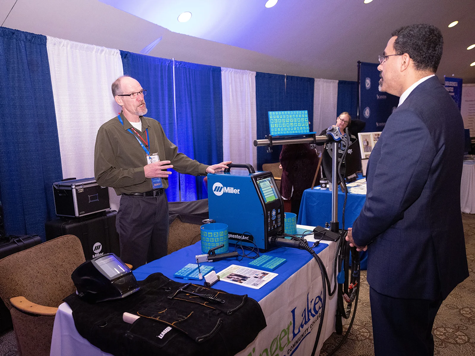 An instructor stands next to a man in a welding helmet using computer simulation technology