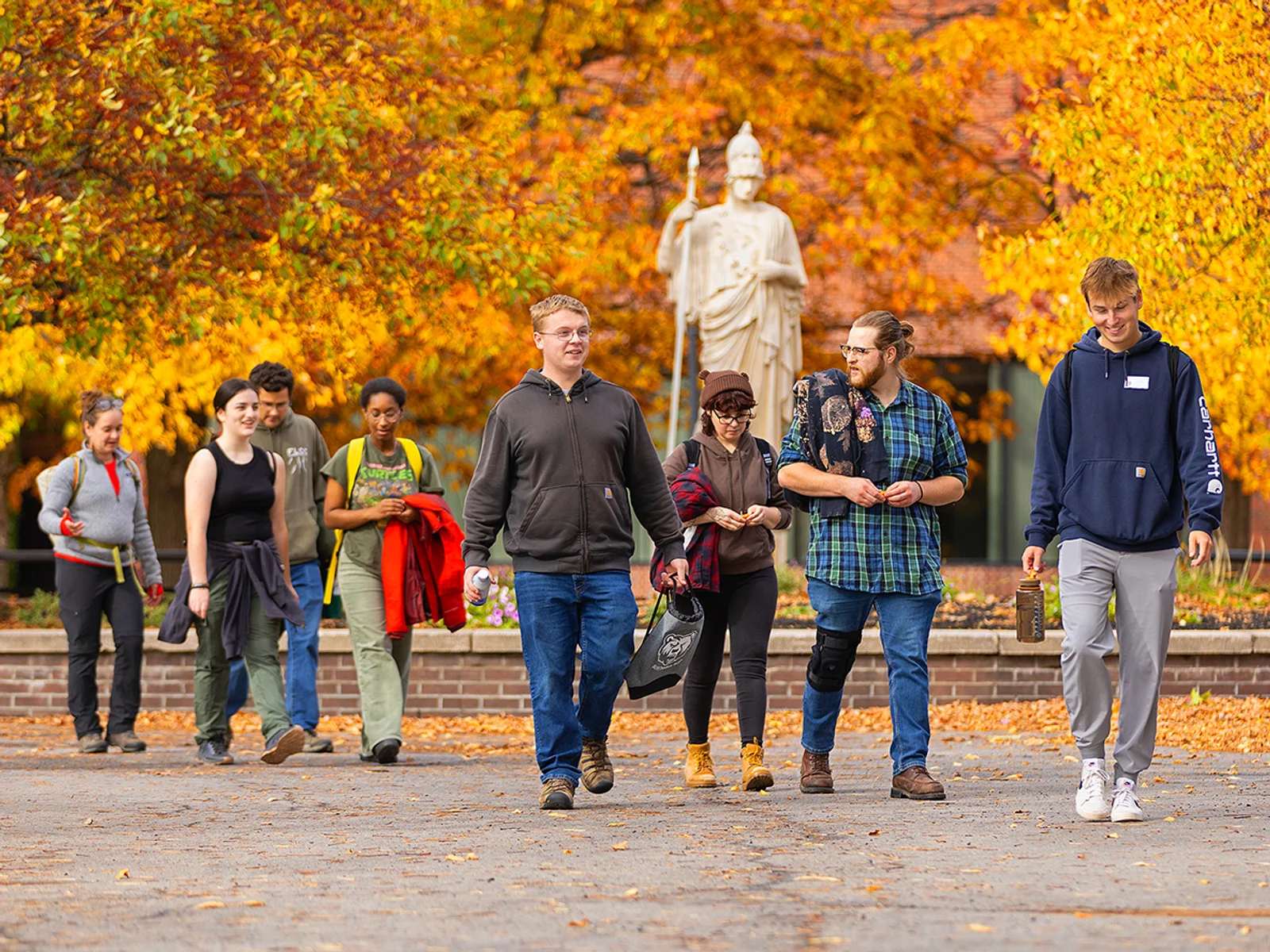 A group of people walking in front of a statue on a fall day