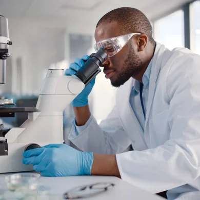 Lab tech looks at a slide through a microscope in the workplace.