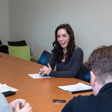 An FLCC student sitting behind a long conference table, sharing a laugh with two others in the room.