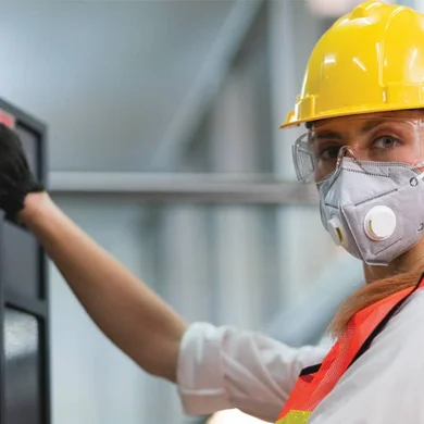 A person in an orange safety vest and hard hat operating manufacturing equipment.