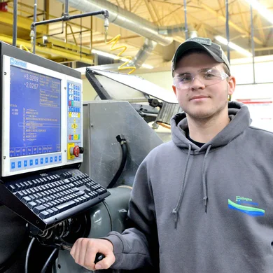 A manufacturing machinist student in front of several pieces of equipment.