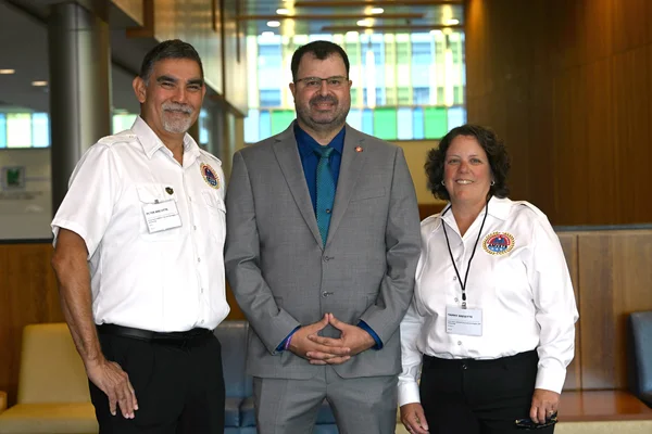 A man in a suit posing between an man and woman in white shirts