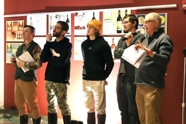 Five individuals standing in a row, watching a presentation. One holds a microphone to ask the presenter a question.