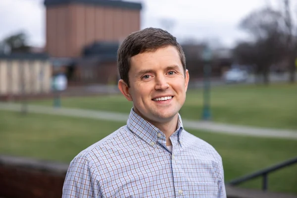 Head and shoulders photo of man in front of college building