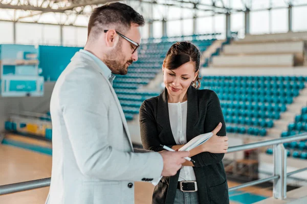 Two Sports Studies students stand in the middle of an empty gymnasium reviewing a playbook together.