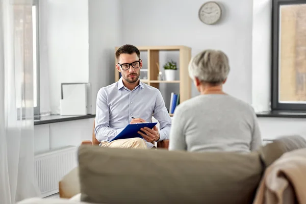 A counselor listens to a patient speaking. The counselor keeps notes of the conversation.