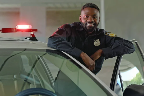 A police officer leans casually against the open door of his squad car, posing for a portrait.