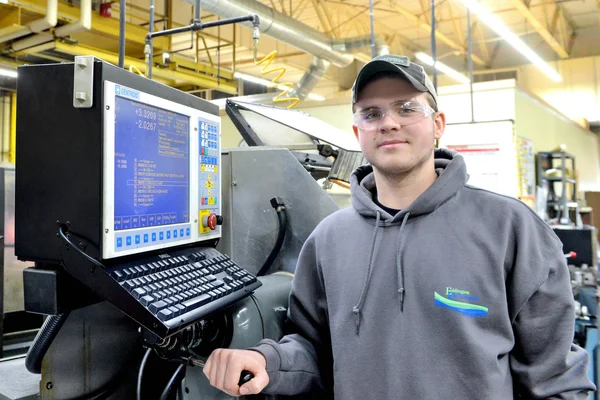 A manufacturing machinist student in front of several pieces of equipment.