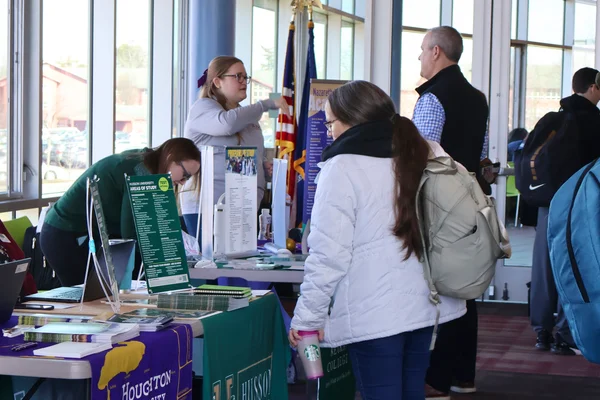 A student stands in front of a table examining informational brochures and discussing transfer options with a representative.