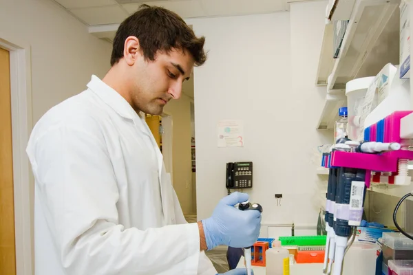 A career training participant in medical lab coat pouring liquid into vials.