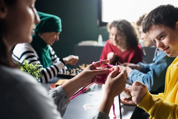 Direct Support Professionals and their clients gathered around a table, knitting, and playing chess.