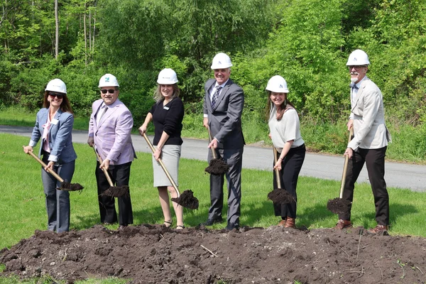 Six individuals holding gold ceremonial shovels for a groundbreaking event.