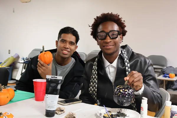 Two students painting pumpkins at an event