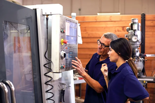 Two individuals working at a machine operating control panel.