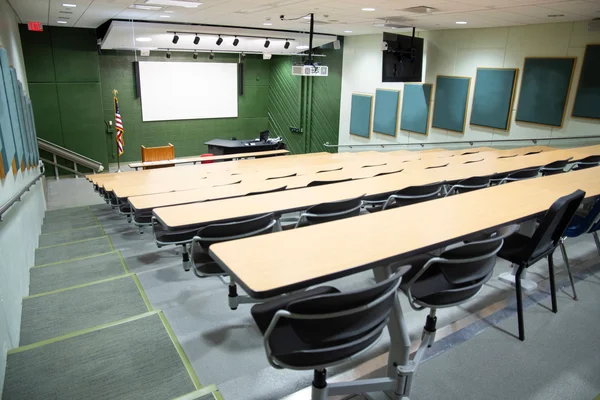 A modern lecture hall at FLCC. Tiered rows of long tables face a large computer display.