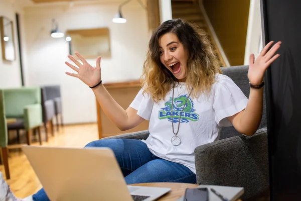 A girl wearing an FLCC lakers t-shirt looking at a laptop in excitement
