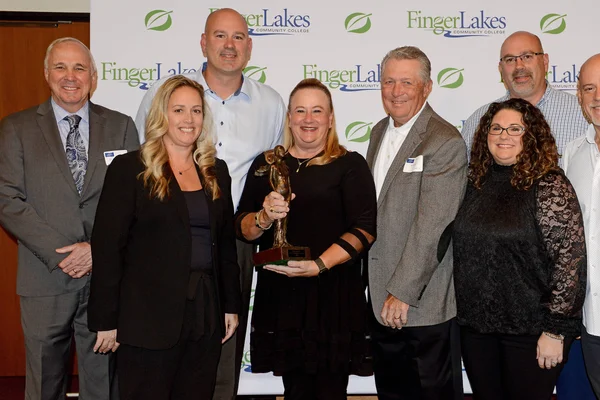 Distinguished Alumni Award winner with trophy in hand stands with FLCC staff.