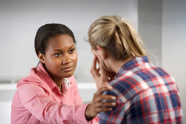 A counselor looks attentively at a woman in distress. She reaches out to gently touch the patient's shoulder.