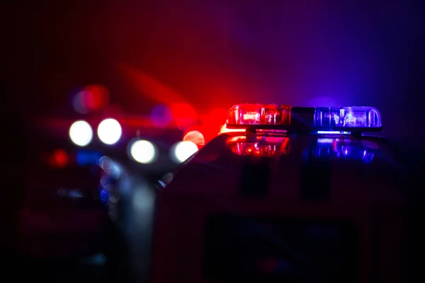 Red and blue police lights shine against a dark, blurred background at the scene of an accident.
