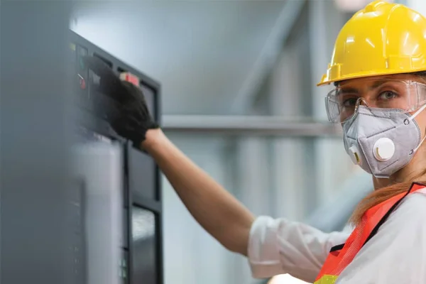 A person in an orange safety vest and hard hat operating manufacturing equipment.