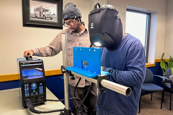 An instructor stands next to a man in a welding helmet using computer simulation technology