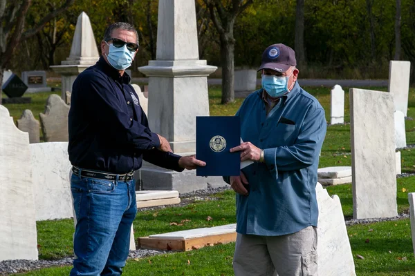 Two men standing in a cemetary holding a plaque