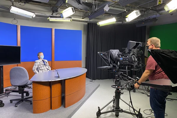 Cameraman filming FLCC student behind desk in TV studio
