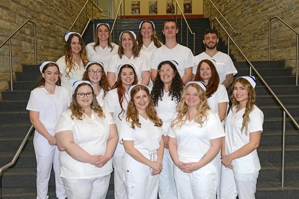 A group photo of 15 nursing graduates in white uniforms