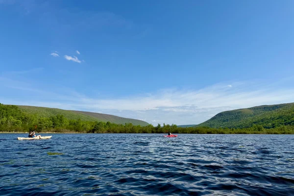 Two people kayaking on lake with green hillsides behind them.