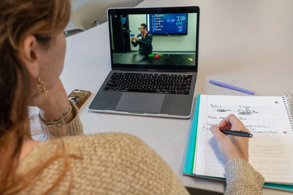A student participating in a synchronous online class, taking notes.