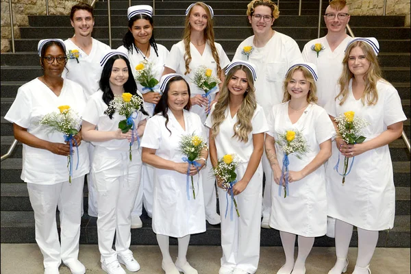 A group of 11 male and female nurses in white uniforms