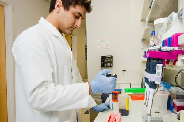 A career training participant in medical lab coat pouring liquid into vials.