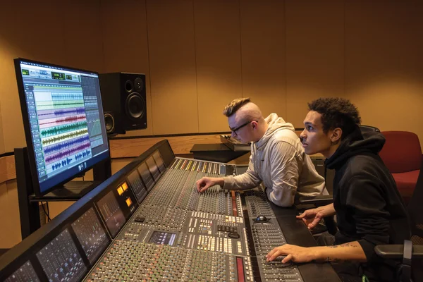 Two music recording technology students adjusting setting on a professional studio soundboard.