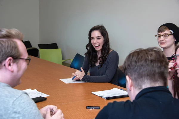An FLCC student sitting behind a long conference table, sharing a laugh with two others in the room.