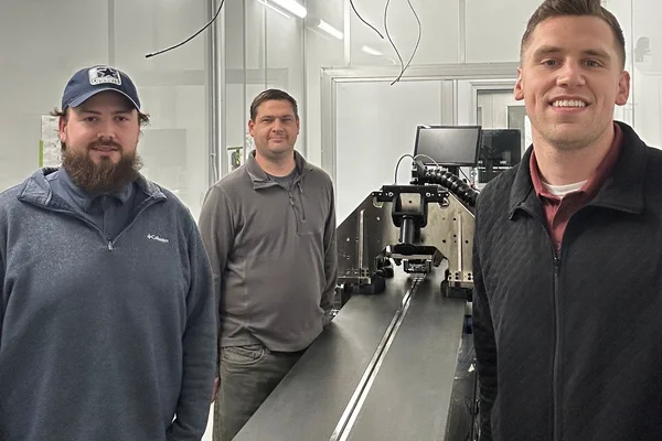 Three men standing next to a long metal table