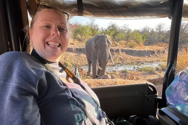 Woman in jeep smiling with elephant in background