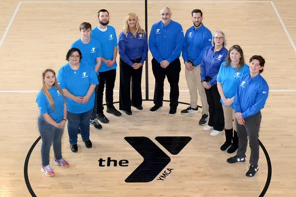 10 people standing in a semicircle around the YMCA logo painted on the gym floor