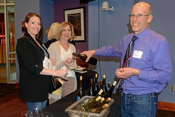 Man standing and pouring wine for 2 women on opposite side of table