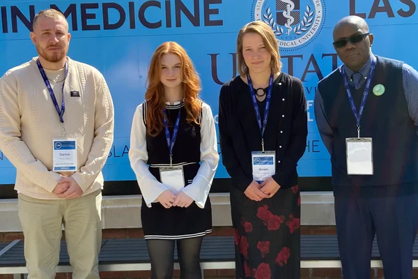 Two men and two women standing in a row wearing conference name tags on lanyards