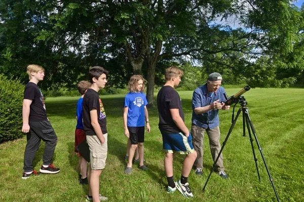 Young students in front of a tree in line to look through a telescope