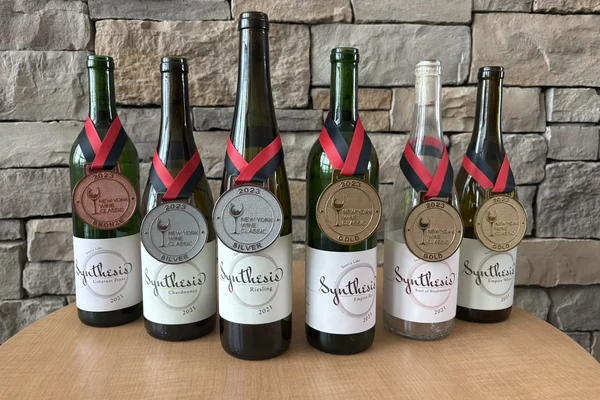 Six bottles of wine from the 2021 vintage, Synthesis, displayed with New York Wine Classic medals.