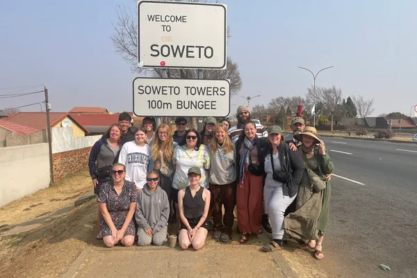 Faculty and students pose for a photo in front of a street sign.