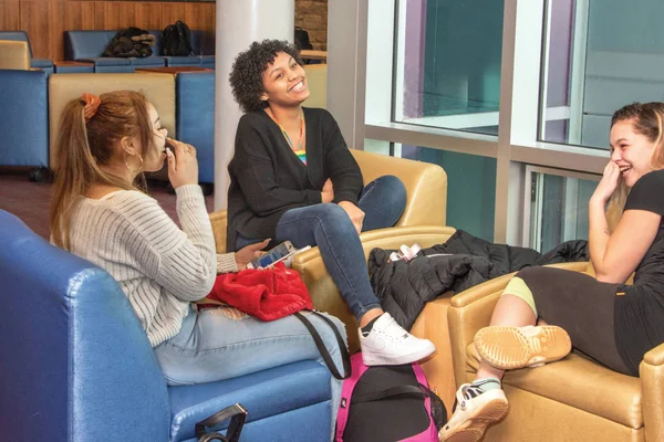 A group of three students relax in a campus lounge, smiling and laughing.