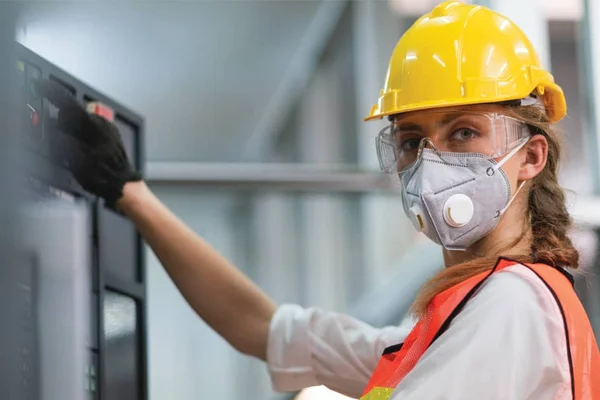 A person in an orange safety vest and hard hat operating manufacturing equipment.