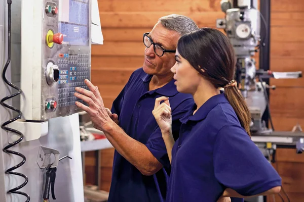 Two individuals working at a machine operating control panel.