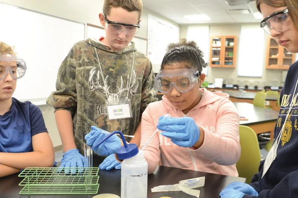 Three students wearing eye protection stand around a lab table as a fourth student uses instruments
