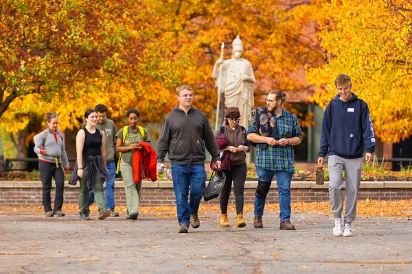 A group of people walking in front of a statue on a fall day